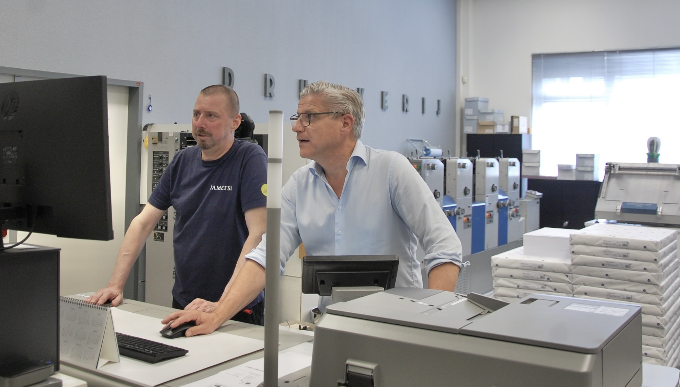 Twee medewerkers bespreken werkzaamheden tussen voertuigen in een professionele werkplaatsomgeving.
