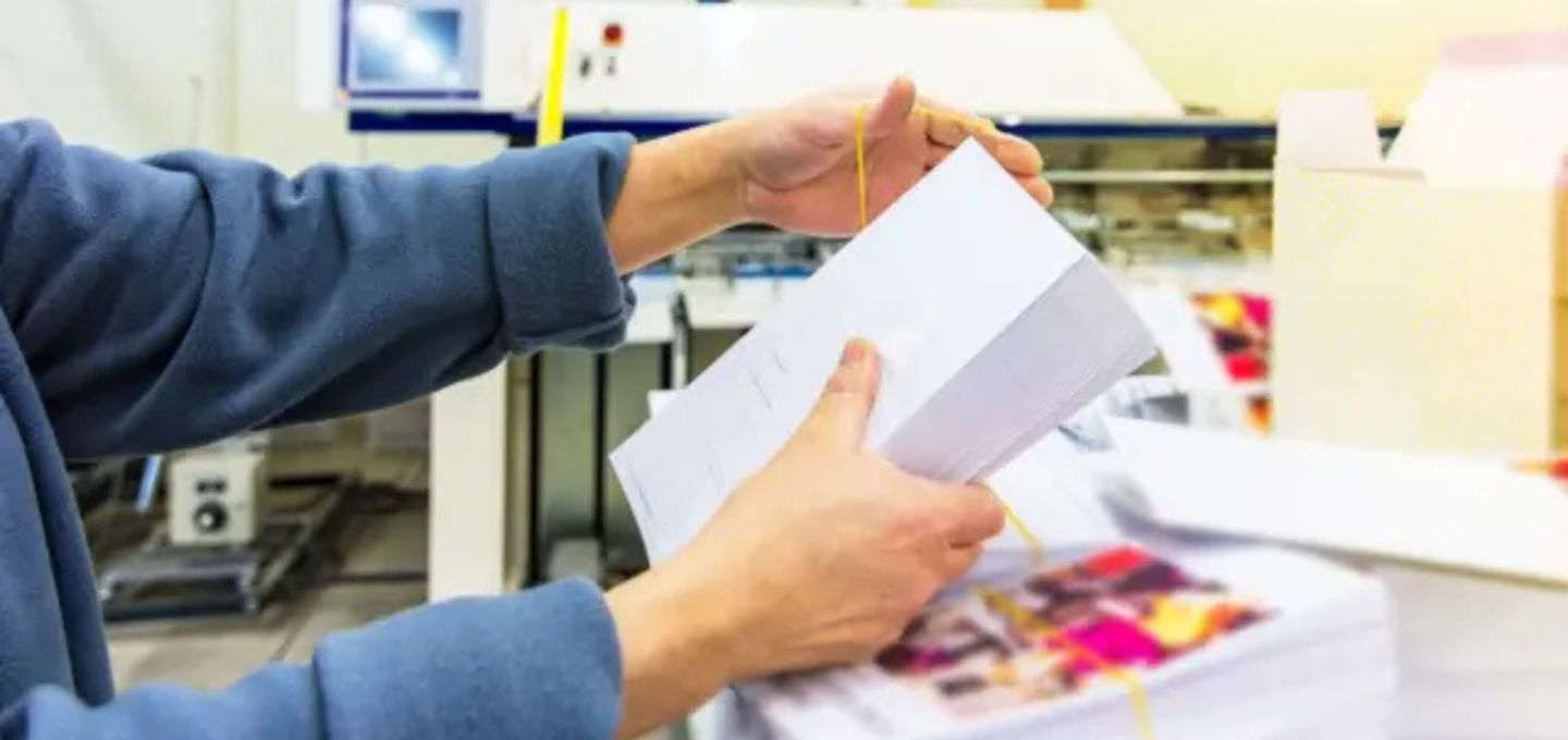 Persoon die typt op een laptop met een smartphone naast zich, met een workflowdiagram dat stappen van een geautomatiseerd printproces weergeeft. 