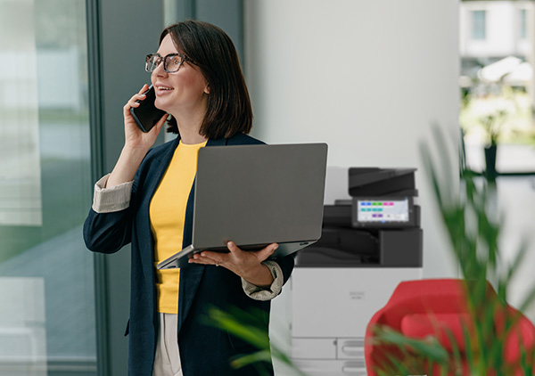Woman holding laptop with printer in the background