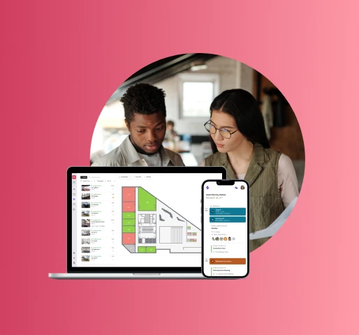 A person with light-colored hair, wearing a light-colored shirt, sits at a wooden desk, working on a laptop in a bright, modern office space. The office has large windows, plants, and a sign that says "RICOH Spaces." The person is looking at the laptop screen.