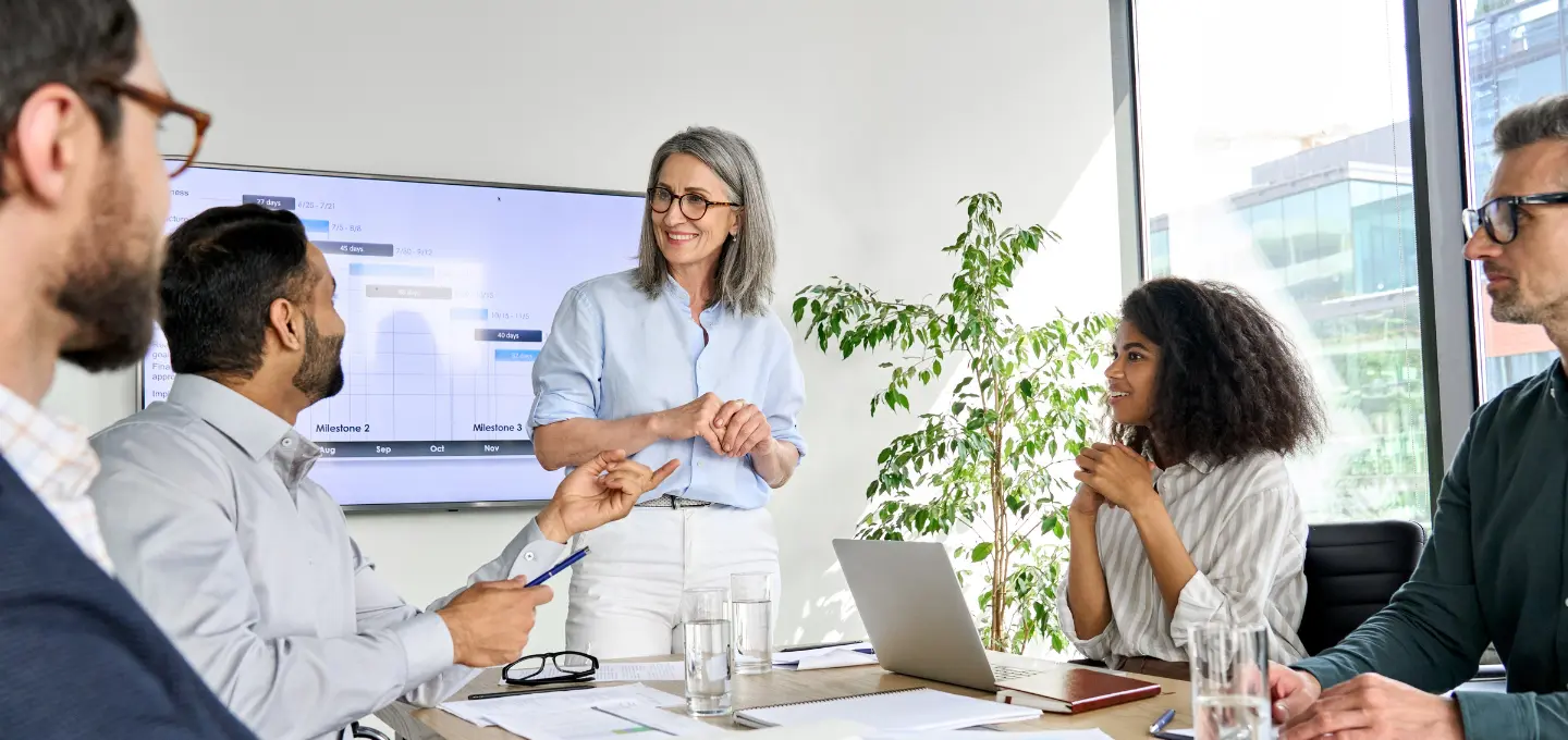 Waar moet een vergaderruimte aan voldoen - 5 mensen zitten en staan in een vergaderruimte, achter hen staat een scherm
