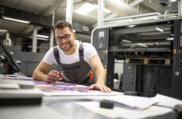 Employee looking at sheets on top of a production printer